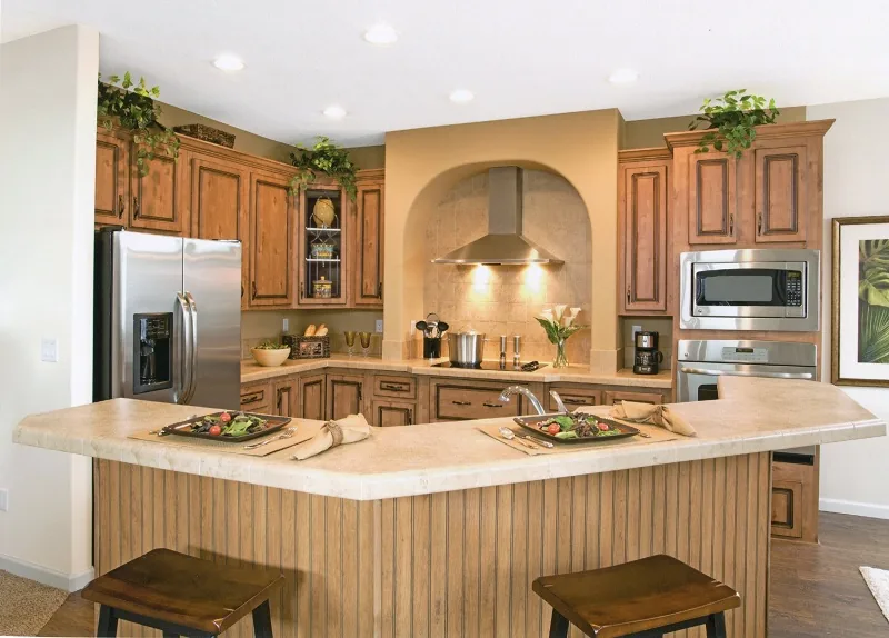 A bright show-home kitchen with an arched range alcove, maple cabinets and a long island with bar stools